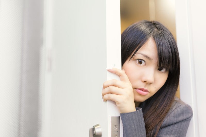 会議の様子をドアの隙間から覗く女性社員の写真