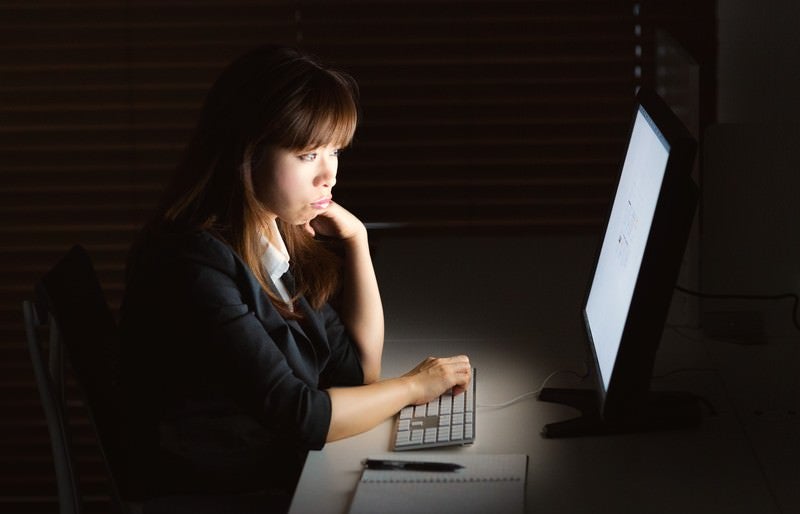 消灯の中、残業してモニターを見つめる女性の写真