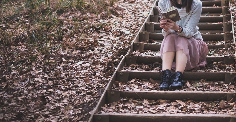 落ち葉が積もる階段で読書に耽る女性の写真