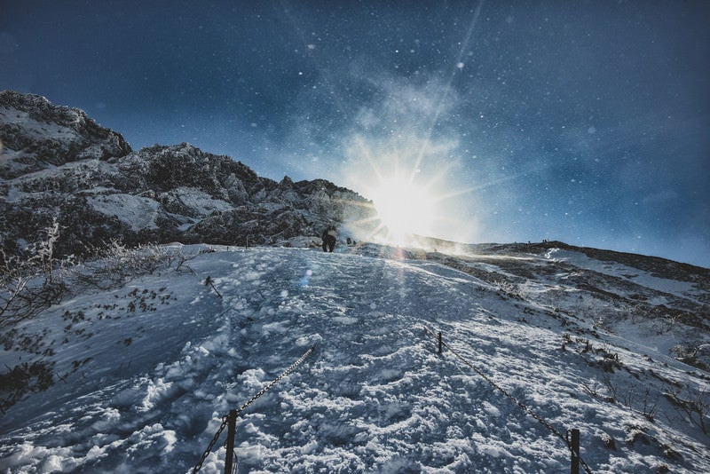 雪煙舞う稜線と登山者の写真