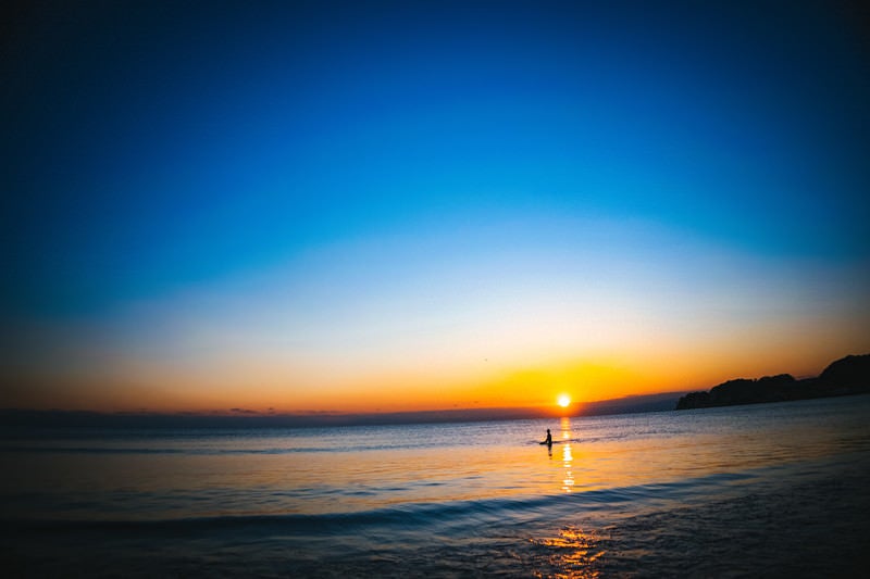 夕日の焼けた海に浮かぶサーファーの写真