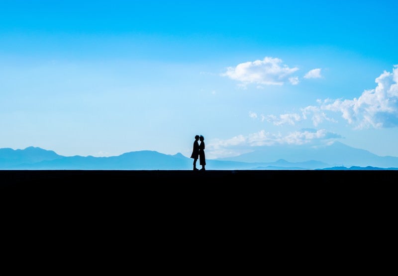 景色のいい堤防の上で顔を近づける恋人の写真