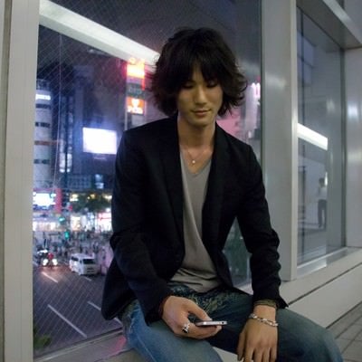 座ってスマホをいじる若者の写真