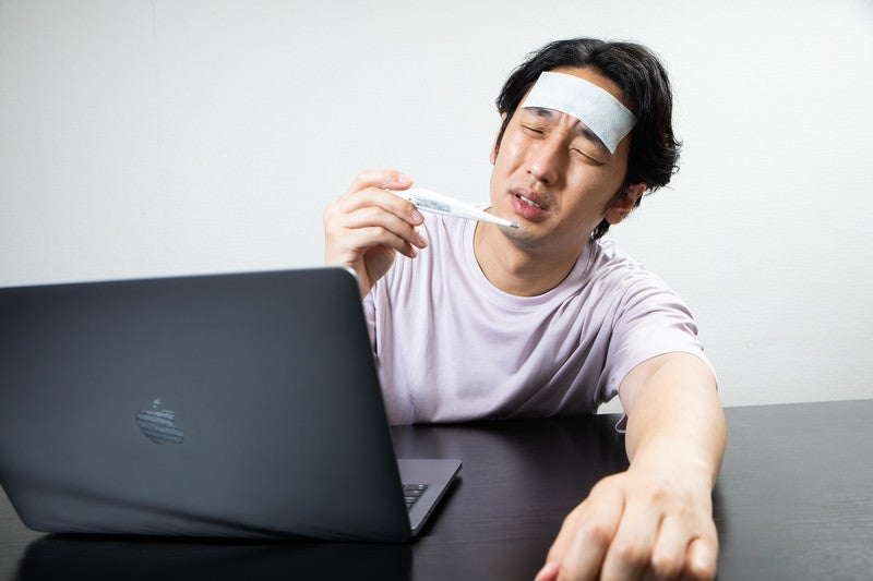 体温計を確認してうなだれる在宅勤務の男性の写真