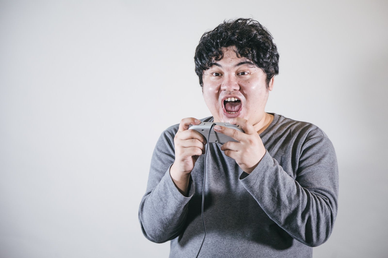 「口を開けて夢中でゲームする男性」の写真［モデル：段田隼人］