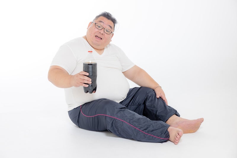 炭酸ジュースを片手に座り込む膨よかな男性の写真