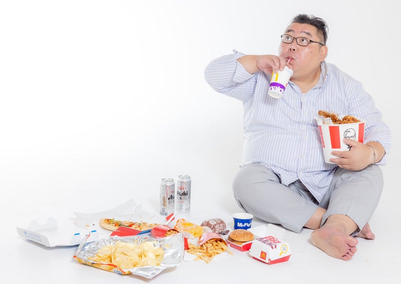 地べたに座ってジャンクフードを暴飲暴食する男性の写真