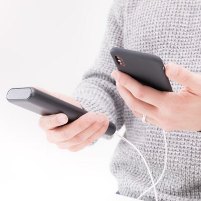 モバイルバッテリーで充電しながらiPhoneを操作する男性の手元の写真