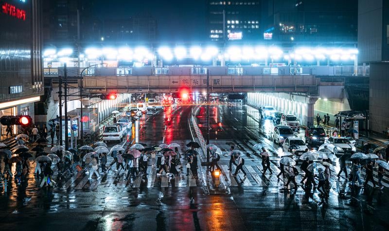 夜の錦糸町駅前の横断歩道を傘を差して横断する人々の写真