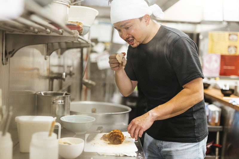 チャーシューをつまみ食いする外国人の店員の写真