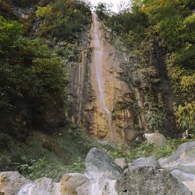 周囲の緑と調和しながら温泉の真上を流れる滝の写真