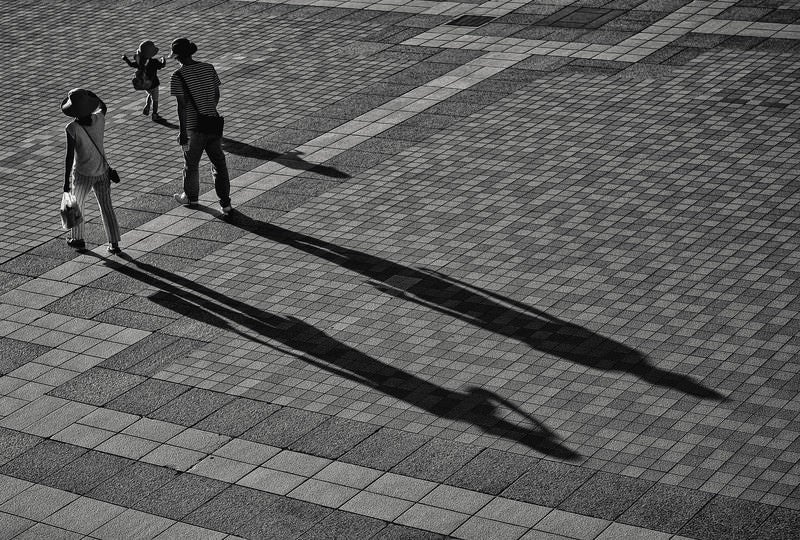 お出かけ中の家族連れと伸びる影の写真