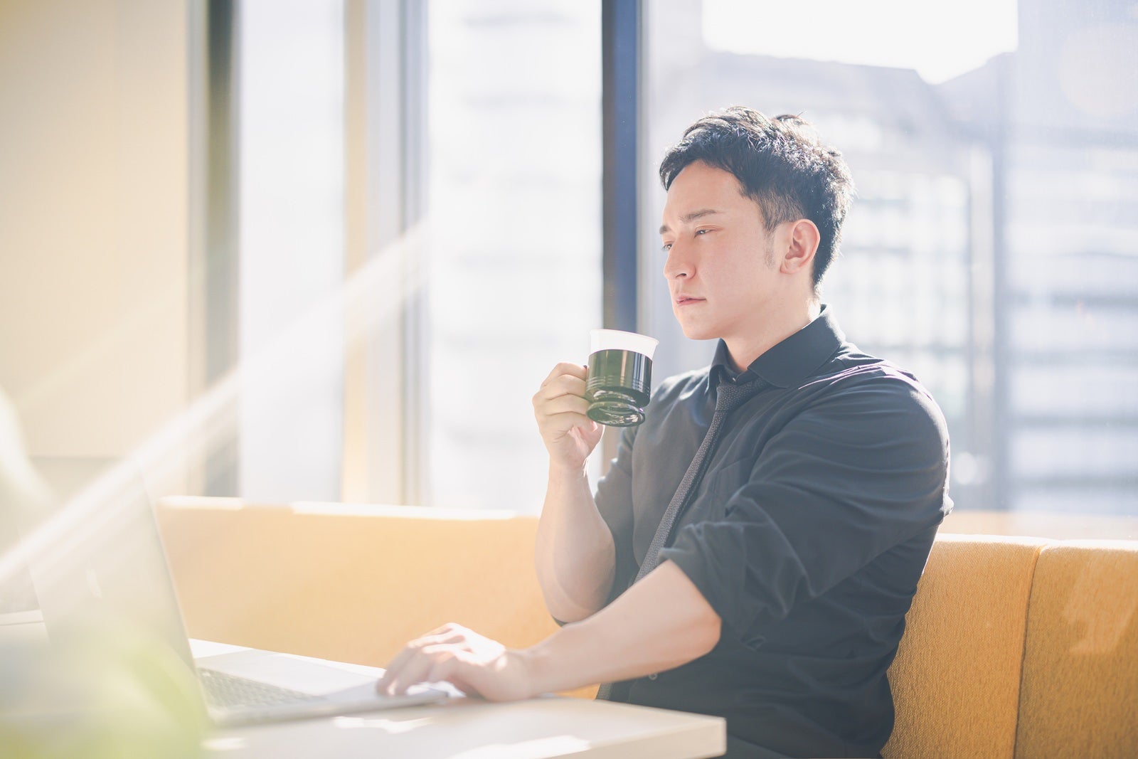 「コーヒーを飲みながらデスクワークをする経営者」の写真［モデル：鈴木秀］