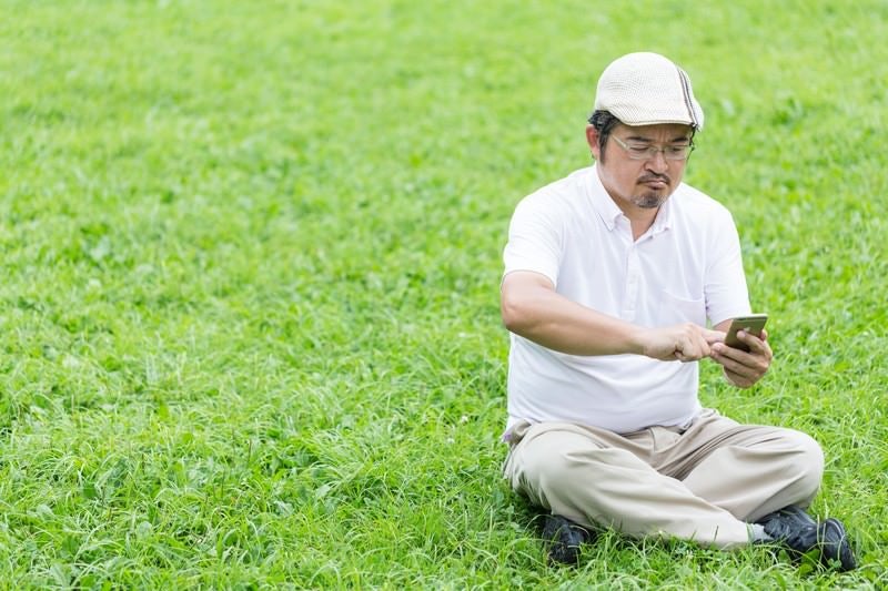 座り込み、ゲームに熱中してしまうハンチング帽の男性の写真